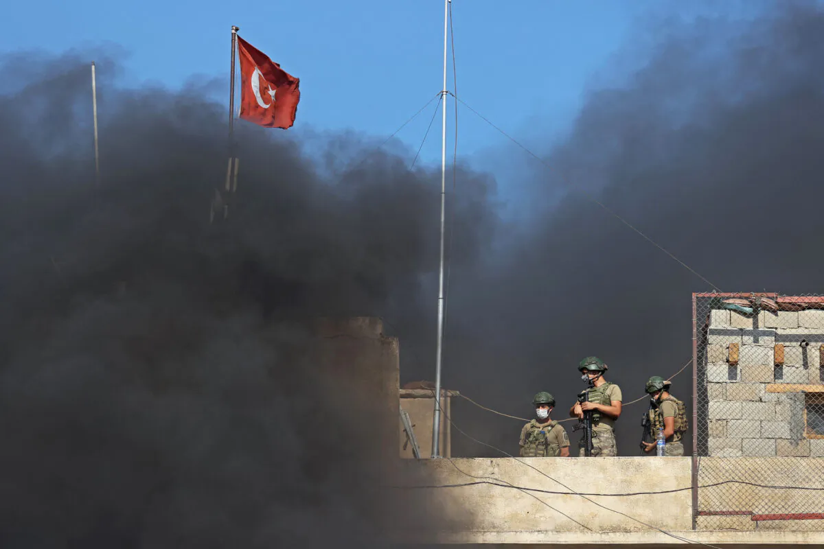 Turkish soldiers stand guard atop an outpost as smoke billows during a demonstration against Ankara's perceived inaction over the latest Syrian regime attacks in Syria's northwestern province of Idlib on July 22, 2021. (Omar Haj Kadour/AFP via Getty Images)