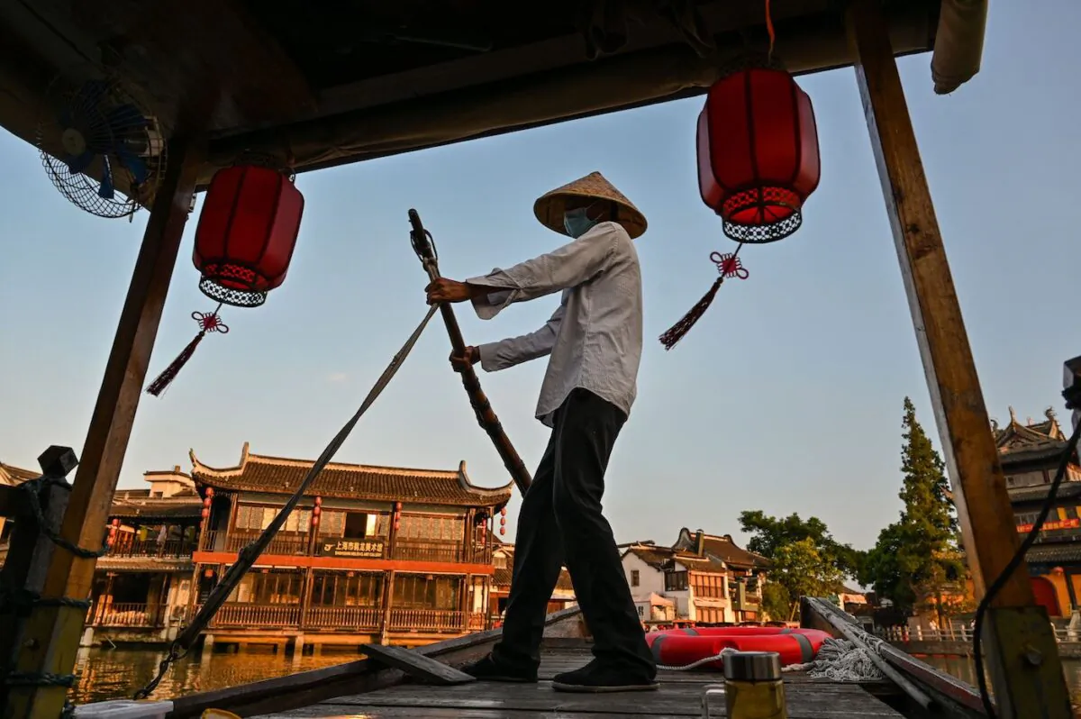 A man is seen sailing a boat with tourists along a channel in the Zhujiajiao ancient water town in Shanghai, on July 31, 2022. (Hector Retamal/AFP via Getty Images)