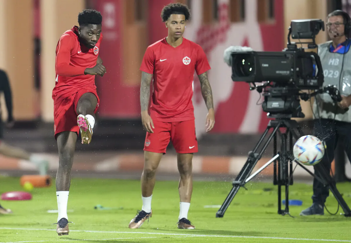 Canada forward Alphonso Davies, left, kicks the ball as teammate Tajon Buchanan, centre, watches during practice at the World Cup in Doha, Qatar on Nov. 22, 2022. (The Canadian Press/Nathan Denette)