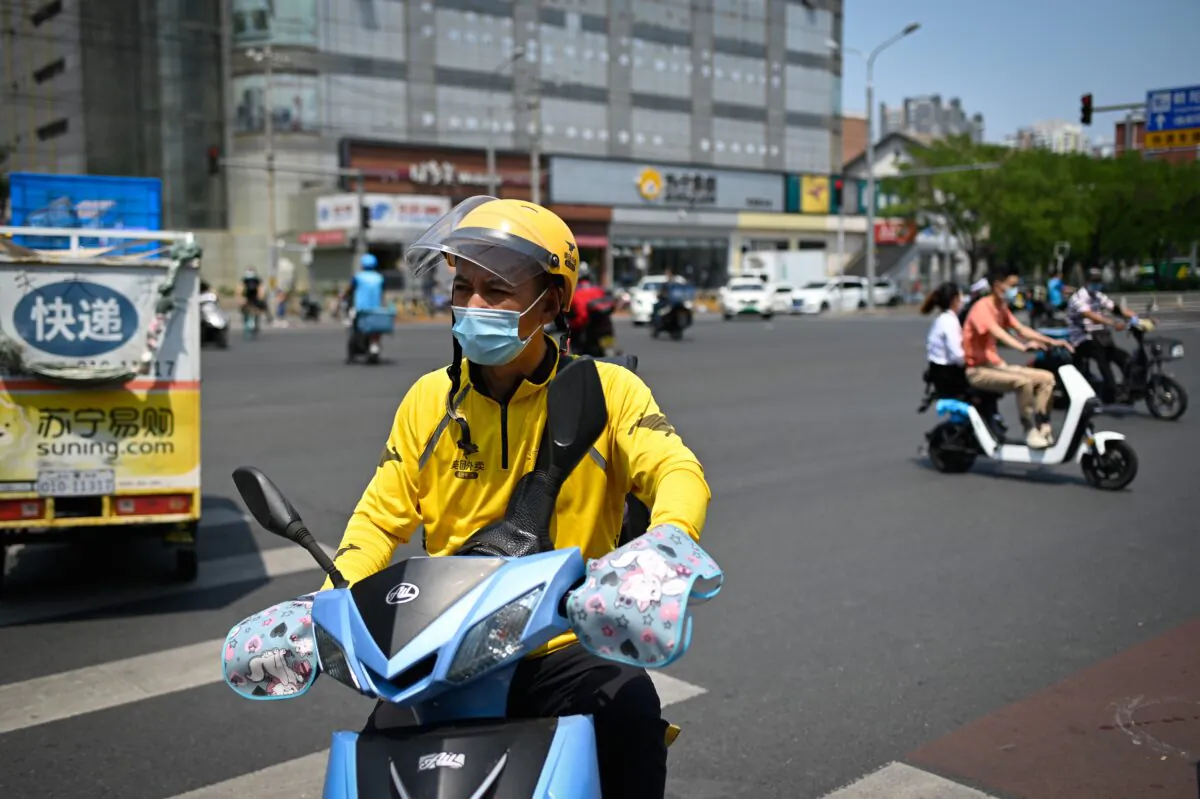 A food delivery driver wearing a face mask rides an electric bicycle across a street in Beijing on June 19, 2020.  (Wang Zhao/AFP via Getty Images)