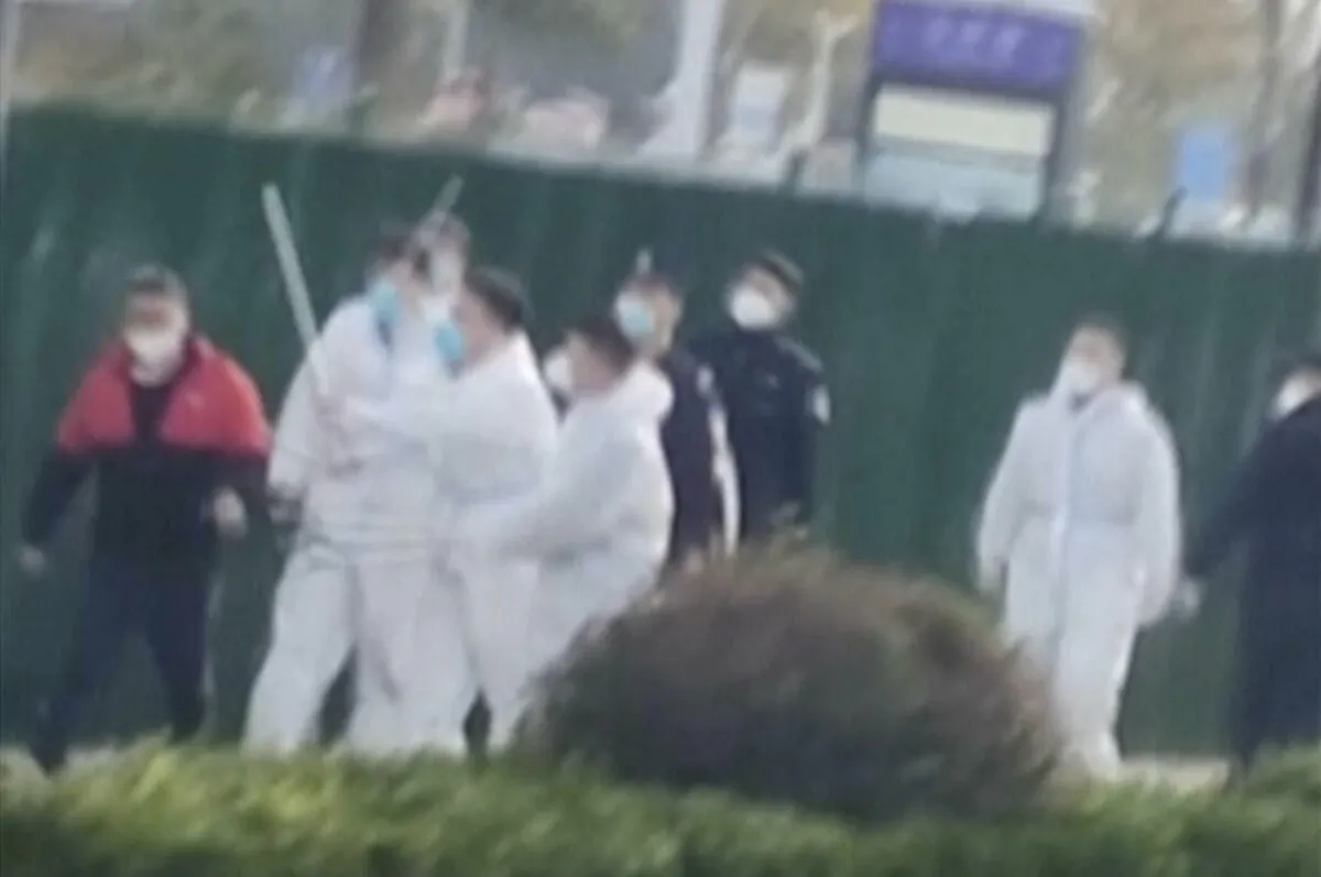 Security personnel in protective clothing attack a protester during protest at the factory compound operated by Foxconn Technology Group who runs the world's biggest Apple iPhone factory in Zhengzhou in central China's Henan province on Nov. 23, 2022. (AP)