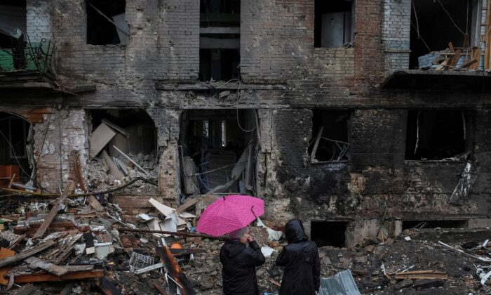 2022 年 11 月 24 日，在乌克兰基辅附近的 Vyshhorod 镇，当地居民站在被俄罗斯导弹袭击摧毁的建筑物附近。（Gleb Garanich / 路透社）