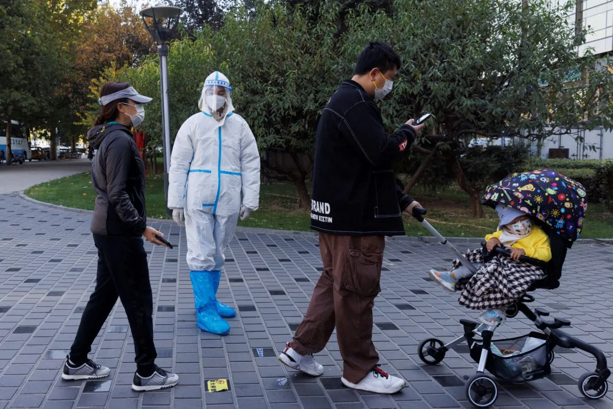 A pandemic prevention worker wears a protective suit as people line up to get swab tests at a testing booth in Beijing on Nov. 3, 2022. (Thomas Peter/Reuters)