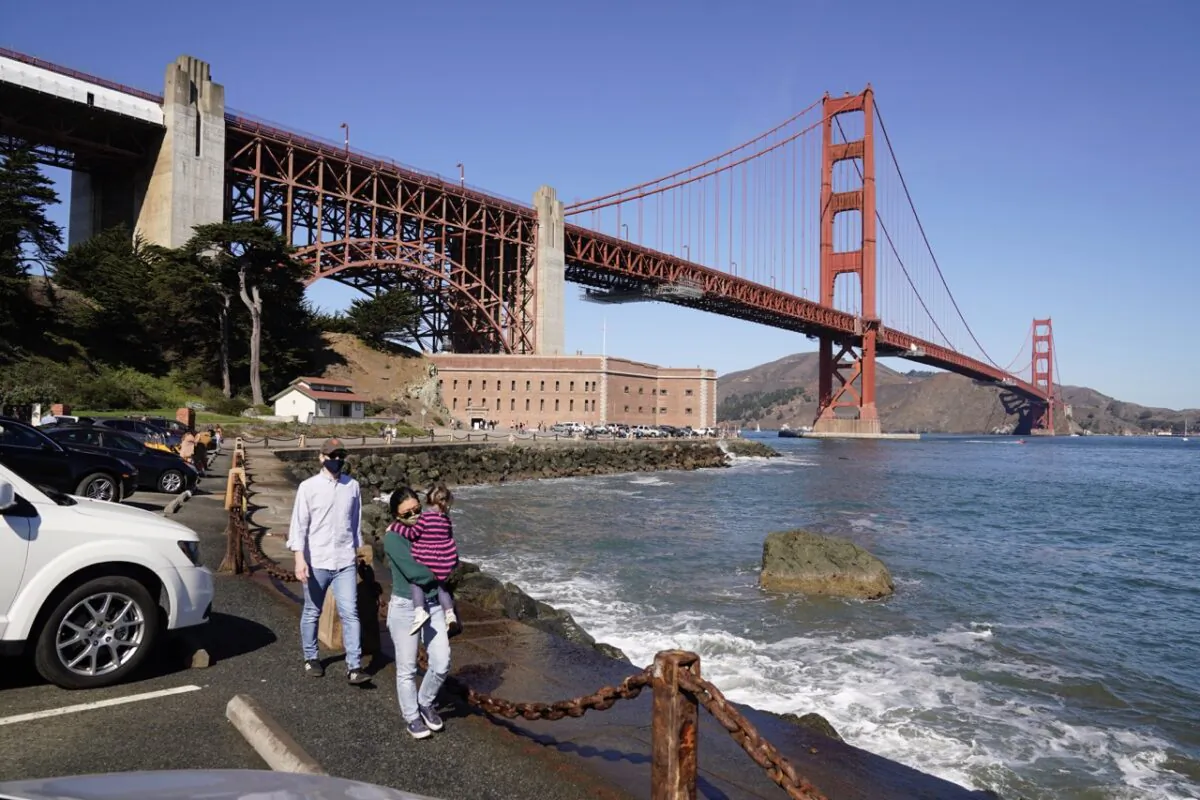 People walk along a seawall with Fort Point and the Golden Gate Bridge in the background in San Francisco on Oct. 11, 2020. (Eric Risberg/AP Photo)