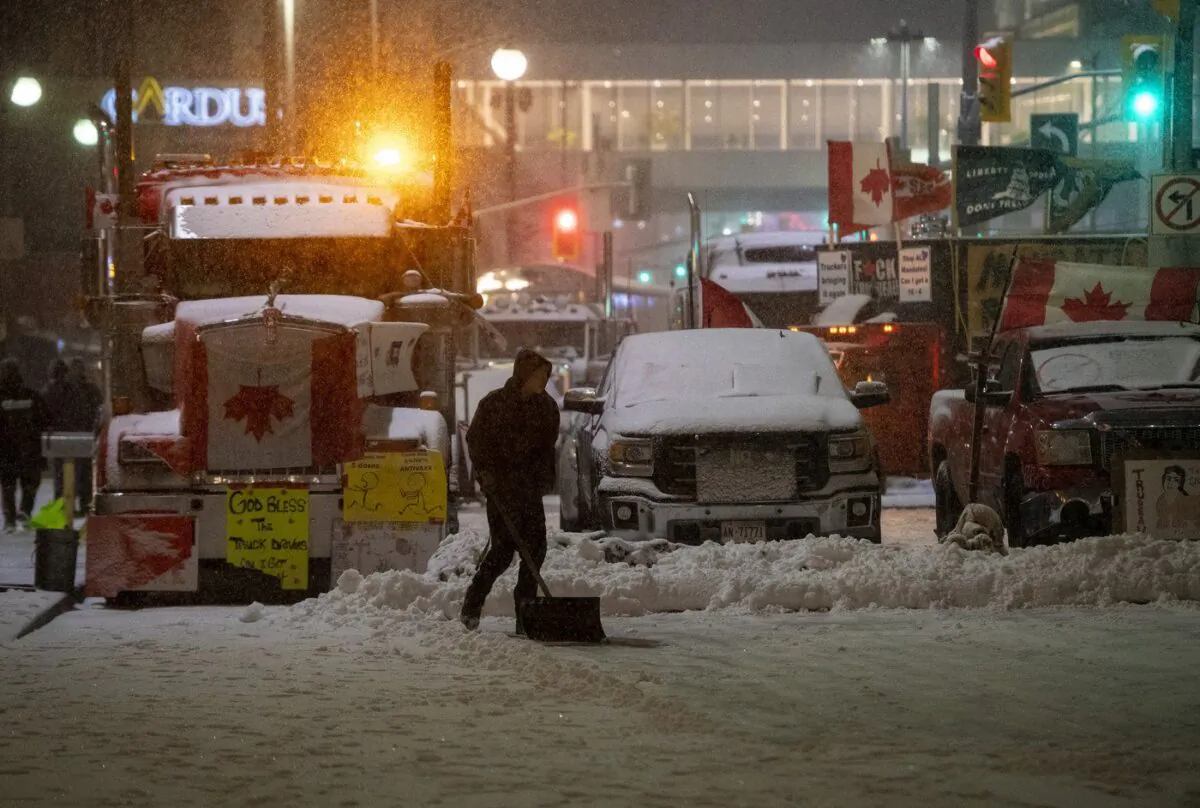 A protester shovels snow in front of parked semi-trailer and pickup trucks on Rideau Street, on the 21st day of a protest against COVID-19 measures that has grown into a broader anti-government protest, in Ottawa, on Feb. 17, 2022. (The Canadian Press/Justin Tang)
