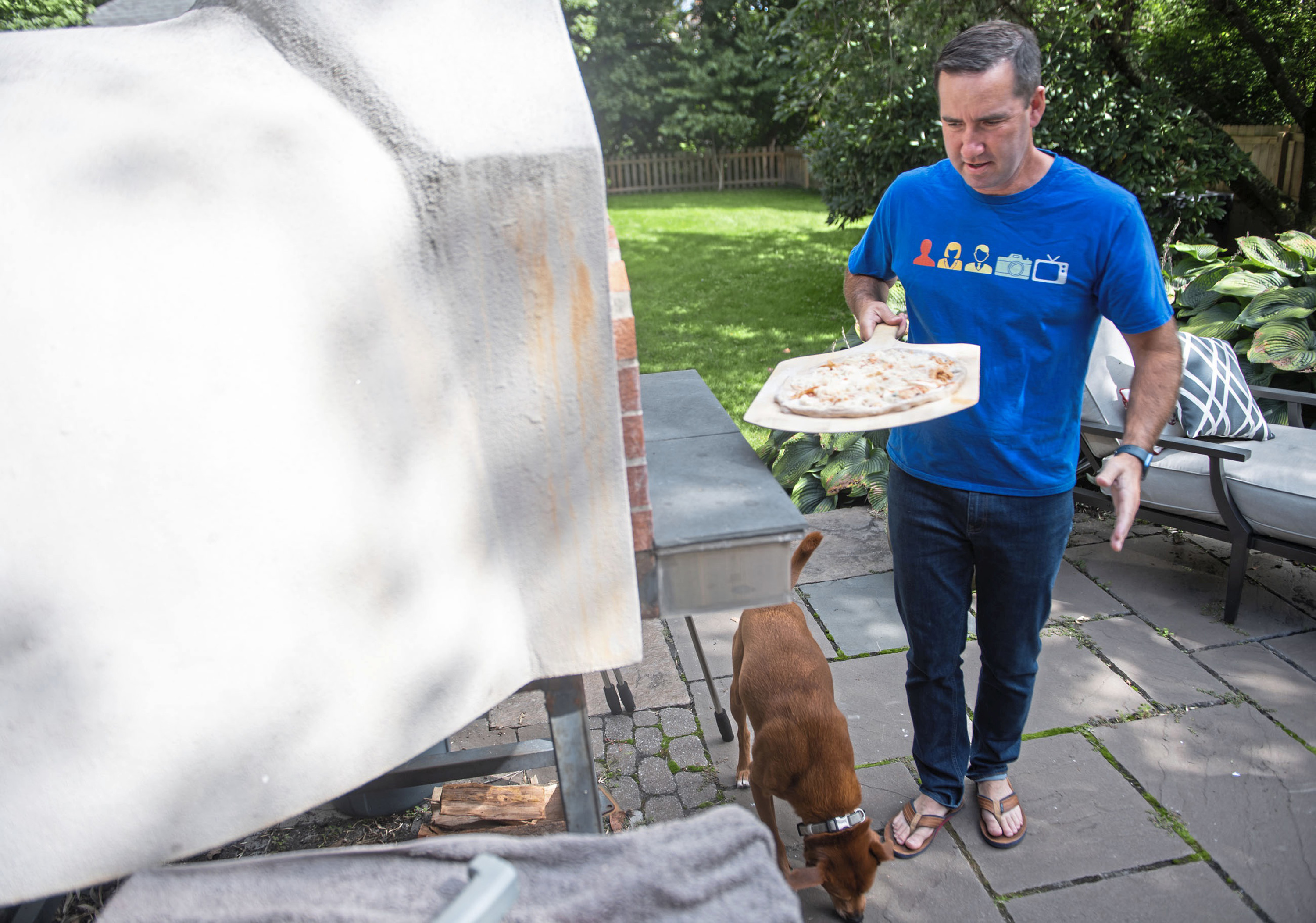 Chris Hayes prepares to put a buffalo chicken pizza in his pizza oven while his dog Charlie looks for any fallen pizza toppings