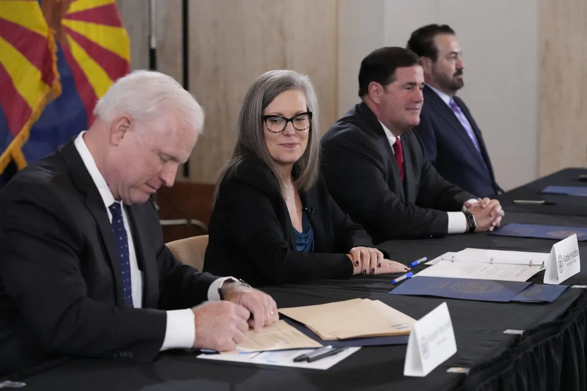 Arizona Supreme Court Chief Justice Robert Brutinel, left, signs the official Arizona general election canvass document as Katie Hobbs, the Democratic governor-elect and current secretary of state, second from left, looks on while Arizona Republican Gov. Doug Ducey, second from right, and Arizona Attorney General Mark Brnovich, right, sit at the table as well during a signing ceremony at the Arizona Capitol in Phoenix, Ariz., on Dec. 5, 2022. (Ross D. Franklin/Pool/AP Photo)
