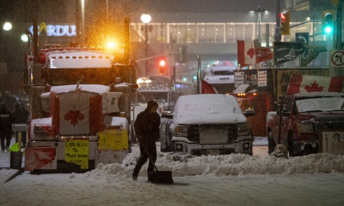 2022 年 2 月 17 日，在渥太华抗议 COVID-19 强制和限制的第 21 天，一名抗议者在里多街停放的半挂车和皮卡车前铲雪。（Justin Tang/加拿大新闻社）