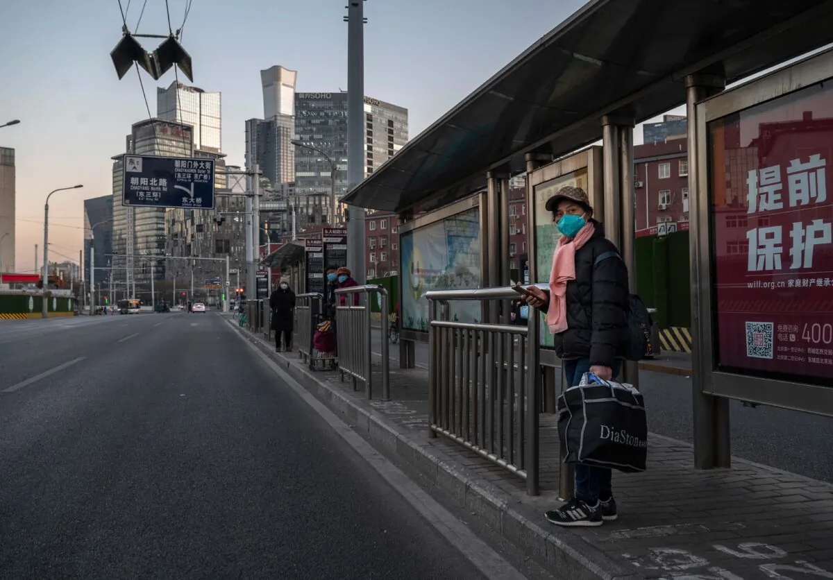 A woman wears a mask to protect against the spread of COVID-19 as she waits at a bus stop on a usually busy street in the Central Business District on December 6, 2022 in Beijing, China. (Kevin Frayer/Getty Images)