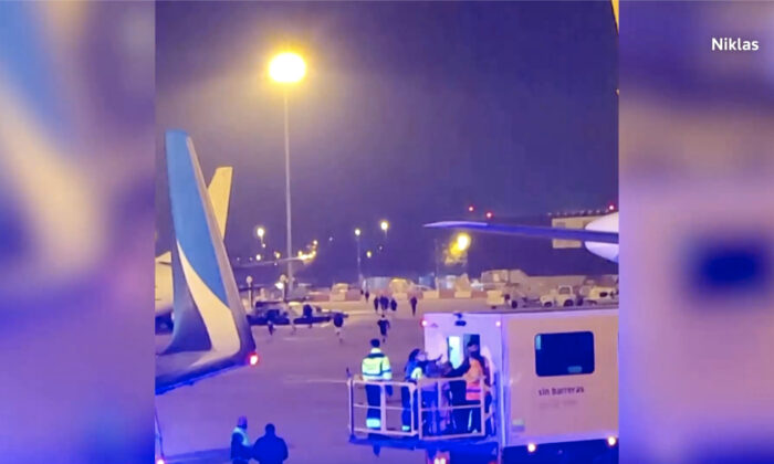 People run across the tarmac at Barcelona's El Prat airport in Spain on Dec. 7, 2022, as emergency services attended a plane. (Courtesy of Niklas via Reuters/Screenshot via NTD)