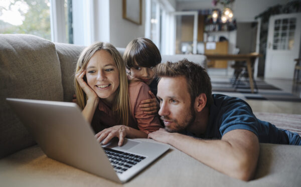 Happy family lying on couch, using laptop