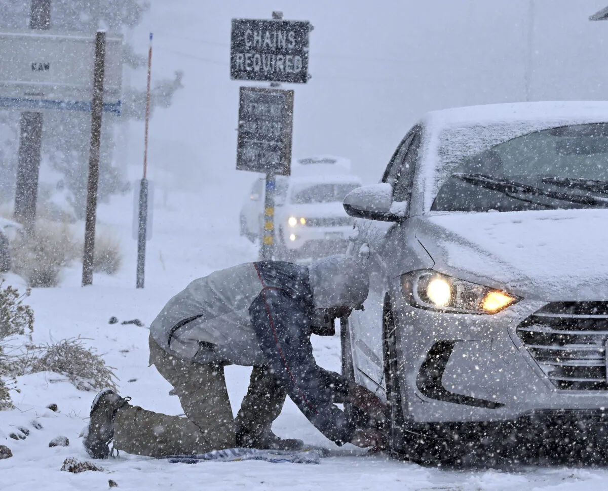 Evan Freedman puts snow chains on his vehicle as heavy snow falls on Highway 2 near Wrightwood, Calif., on Dec. 12, 2022. (Will Lester/The Orange County Register via AP)