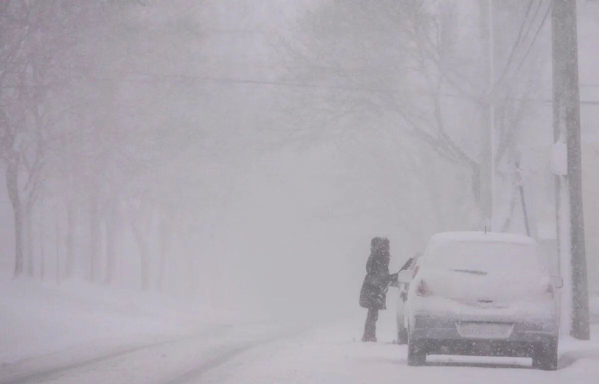 In this file photo a woman cleans snow off her car as a storm brings white-out conditions to Halifax on Mar. 8, 2018. (The Canadian Press/Darren Calabrese)

