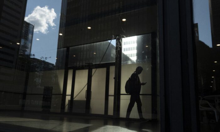 在这张 2019 年 6 月 11 日的照片中，一名男子走过多伦多市中心的一栋办公楼，窗户中倒映着其他建筑物。  （加新社/Graeme Roy）
