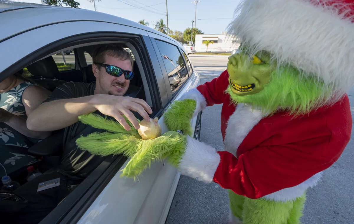 A Maryland motorist (L) accepts an onion instead of a traffic citation from Monroe County Sheriff's Office Colonel Lou Caputo (R), costumed as the Grinch, in Marathon, Fla., on Dec. 13, 2022. (Andy Newman/Florida Keys News Bureau via AP)