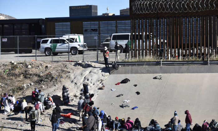 2022 年 12 月 14 日，星期三，在得克萨斯州埃尔帕索，非法移民等待从 Ciudad Juárez 越过美墨边境，旁边是美国边境巡逻车。（美联社照片/Christian Chavez）