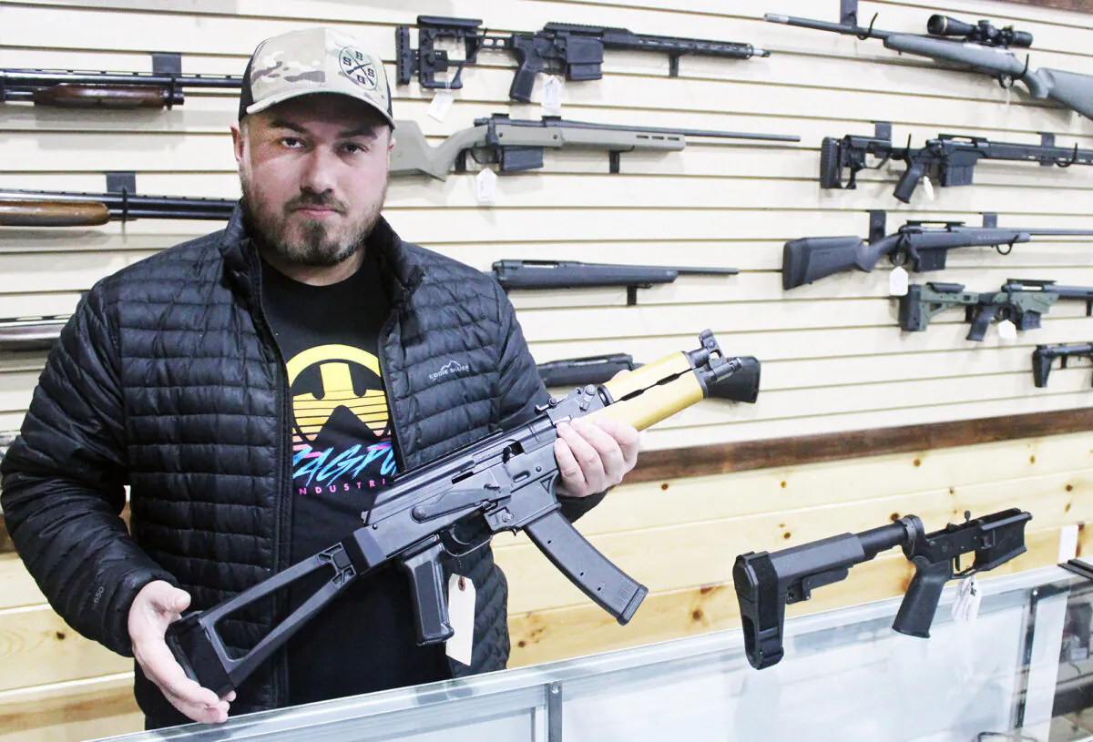 Justin Barrett, owner of Barrett Outdoors in Durant, Okla., displays an AK pistol with a stabilizing brace. On the counter next to him is a similar brace for an AR15 pistol. (Michael Clements/The Epoch Times)