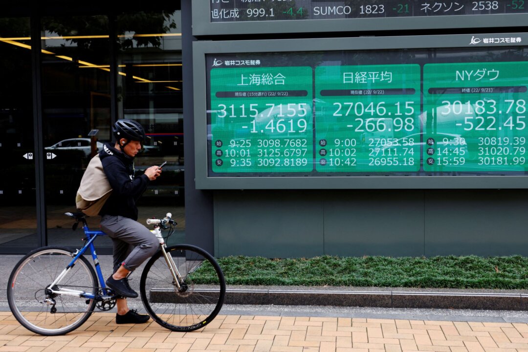 A man on a bicycle stands in front of an electronic board showing Shanghai stock index, Nikkei share price index, and Dow Jones Industrial Average outside a brokerage in Tokyo on Sept. 22, 2022. (Kim Kyung-Hoon/Reuters)