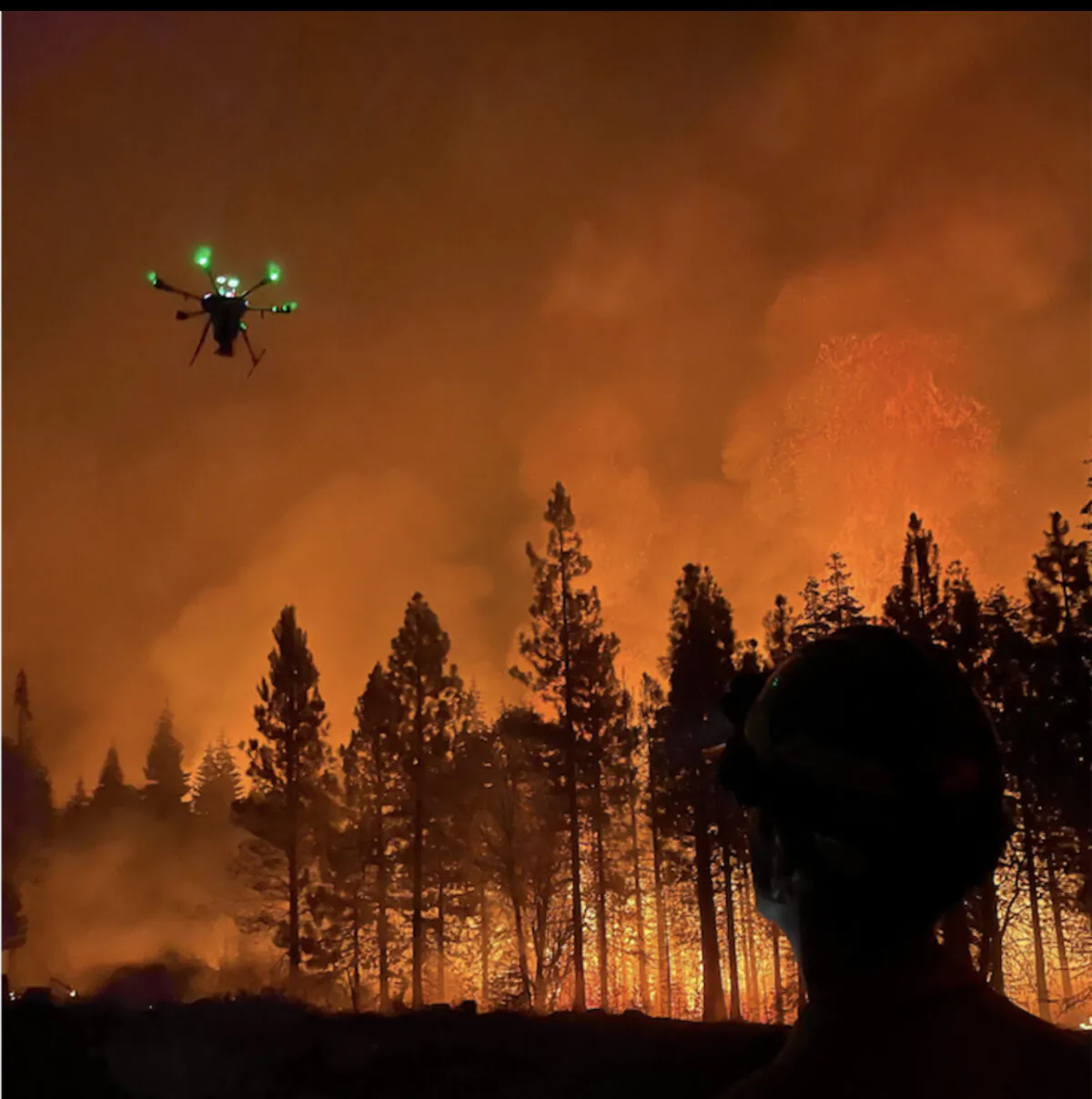 A firefighting drone flies near a fire. (Drone Amplified)
