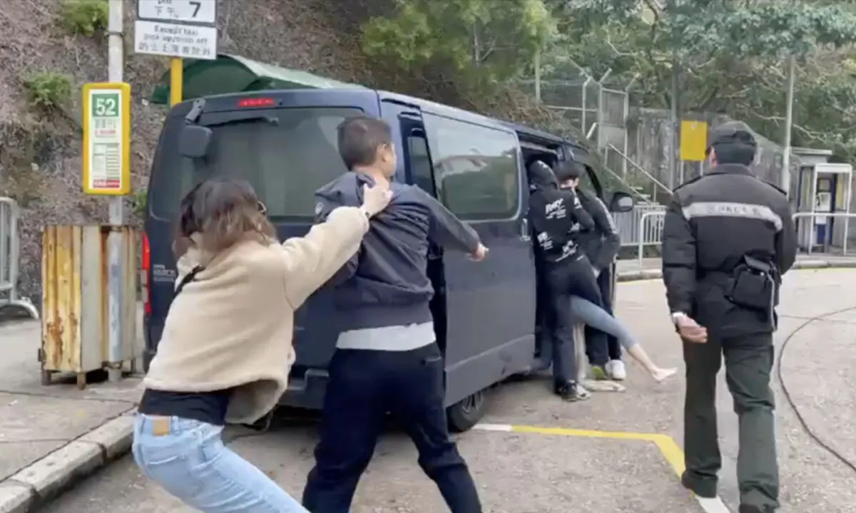 In this still taken from video a good samaritan and correctional officer are seen trying to stop a woman from being forcibly taken into a van at Stanley Prison in Hong Kong on Dec. 17, 2022. (Screenshot via the Epoch Times)