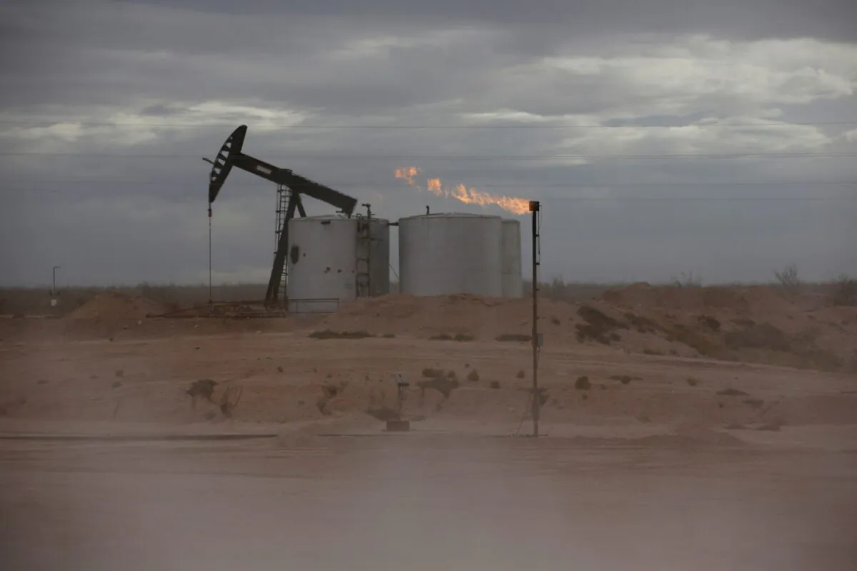Dust blows around a crude oil pump jack and flare burning excess gas at a drill pad in the Permian Basin in Loving County, Texas, on Nov. 25, 2019. (Angus Mordant/Reuters)
