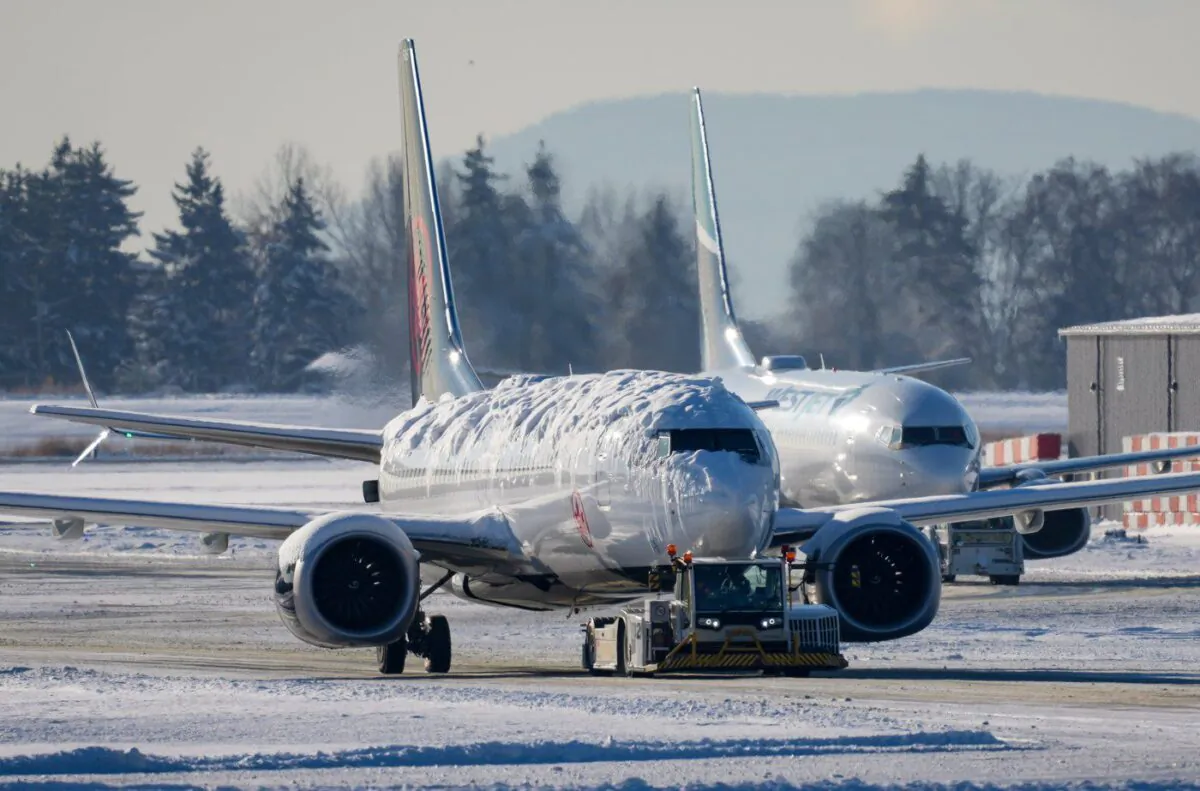 An Air Canada aircraft covered with snow and ice is moved by a tug as a Westjet aircraft is seen being moved behind it at Vancouver International Airport in Richmond, B.C., on Dec. 21, 2022. (The Canadian Press/Darryl Dyck)