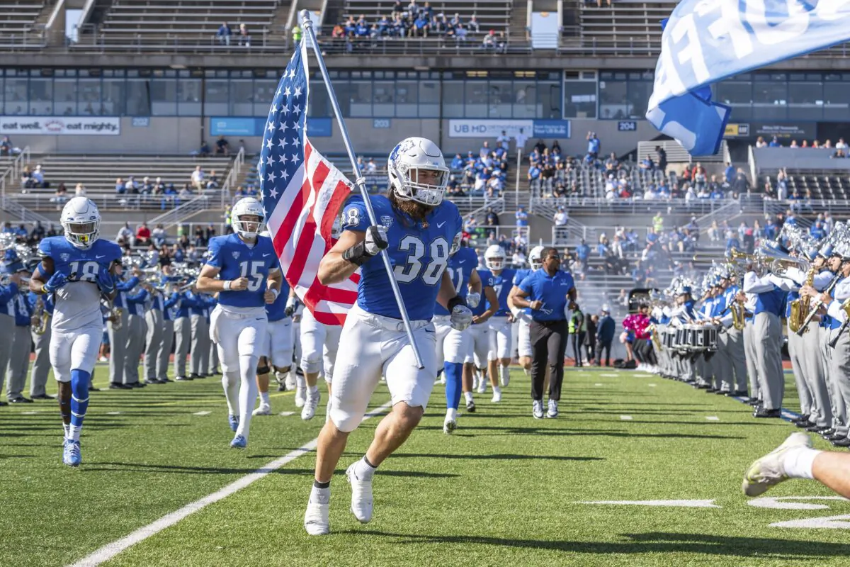 University of Buffalo NCAA college football player Damian Jackson (38) carrying the American flag as the team takes the field before a game against Toledo, in Buffalo, N.Y., on Oct. 22, 2022. (Paul Hokanson/Univ. of Buffalo Athletics via AP)