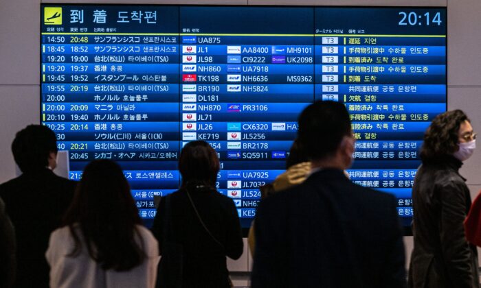 People wait in front a board showing international flight arrivals at Tokyo's Haneda international airport on Dec. 28, 2022. (Philip Fong/AFP via Getty Images)