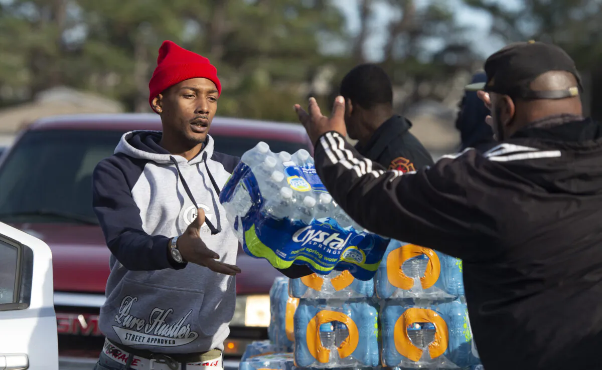 Dontavious Spann (L) with the Mississippi Rapid Response Coalition, and volunteer Preston Alston of Jackson, Miss., help to distribute water to Jackson residents near Northside Drive and Manhattan Road on Dec. 27, 2022. (Barbara Gauntt/The Clarion-Ledger via AP)
