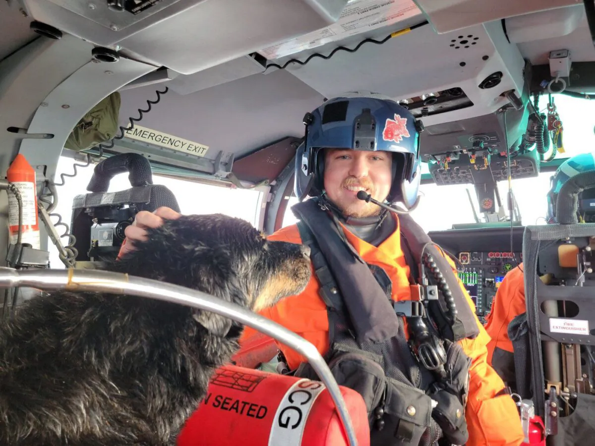 An unidentified member of the United States Coast Guard Air Station Port Angeles aircrew pets a dog on board his helicopter after the dog was airlifted from a sailboat that had washed onto rocks off Vancouver Island in a Dec. 28, 2022, handout photo. (The Canadian Press/HO-United States Coast Guard)
