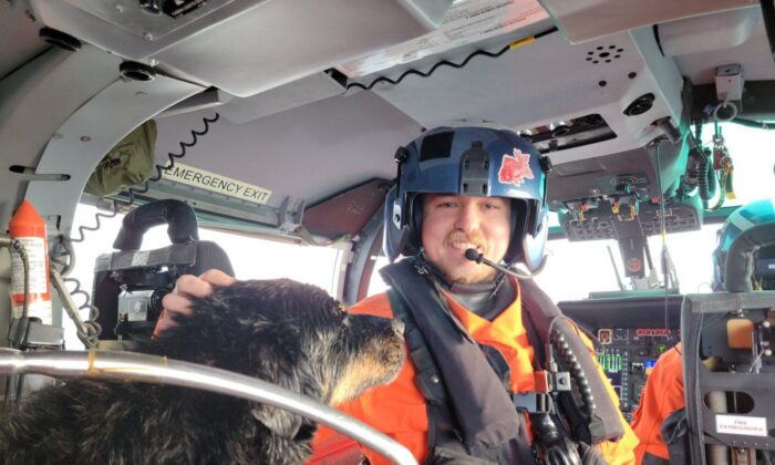 An unidentified member of the United States Coast Guard Air Station Port Angeles aircrew pets a dog on board his helicopter after the dog was airlifted from a sailboat that had washed onto rocks off Vancouver Island in a Dec. 28, 2022, handout photo. (The Canadian Press/HO-United States Coast Guard)
