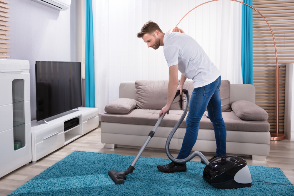 Young,Man,Cleaning,Blue,Carpet,With,Vacuum,Cleaner,At,Home