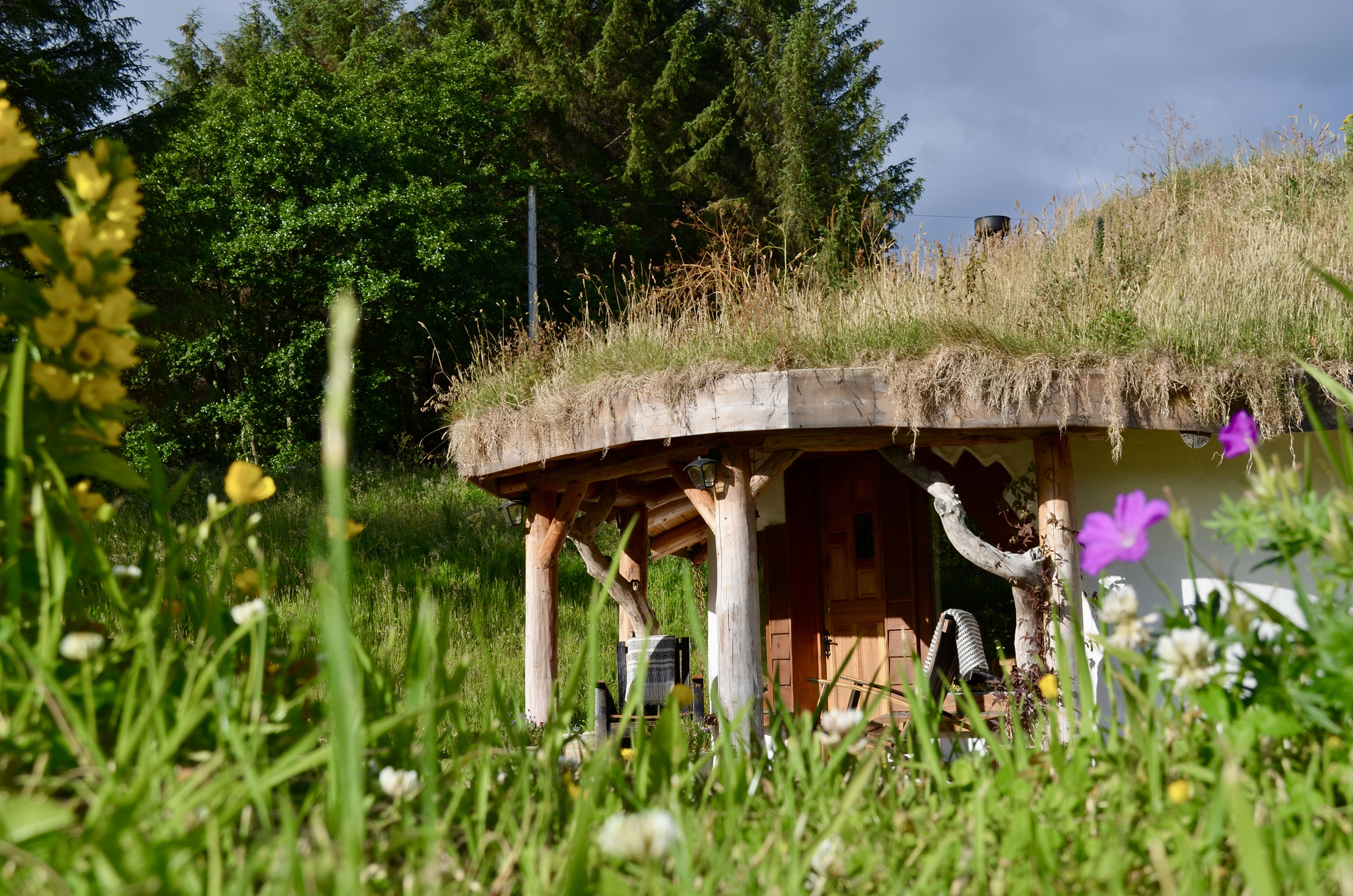 An outside view of The Hideaway Under the Stars showing flowers and a grass roof