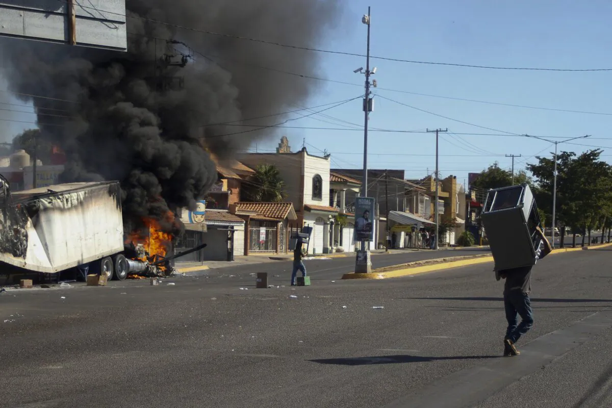 Men carry furniture after looting a store, as a truck burns on a street in Culiacan, Sinaloa state, Jan. 5, 2023. (The Canadian Press/AP-Martin Urista)