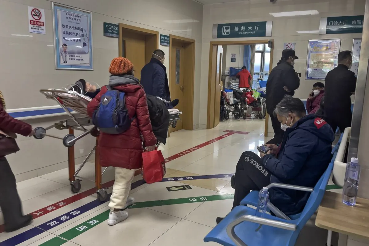 A man (R) browses his smartphone on a bench as an elderly patient is wheeled to an emergency hall in a hospital in Beijing on Jan. 7, 2023. (Andy Wong/AP Photo)