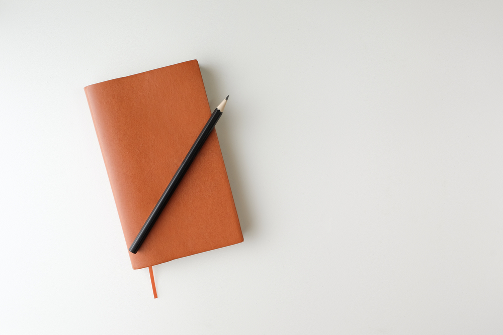 Top,View,Blank,Orange,Leather,Diary,And,Pencil,On,White