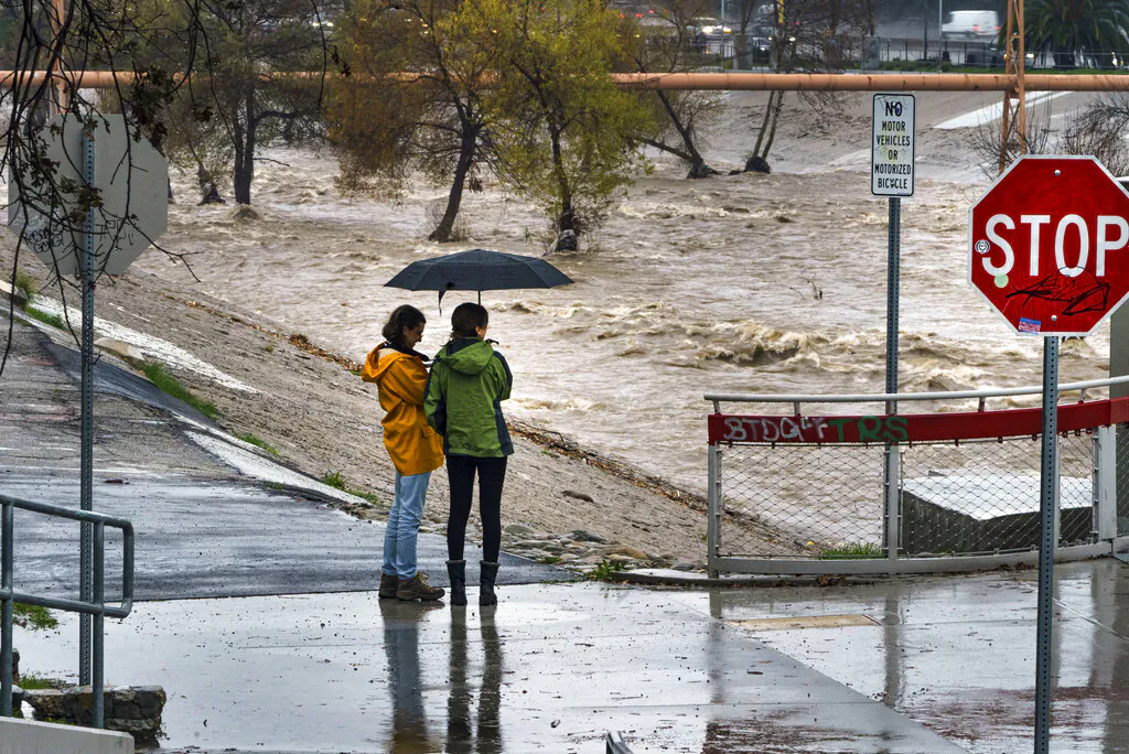 People watch the high volume of storm rain water flowing downstream at the Los Angeles River in Los Angeles on Jan. 14, 2023. (Damian Dovarganes/AP Photo)