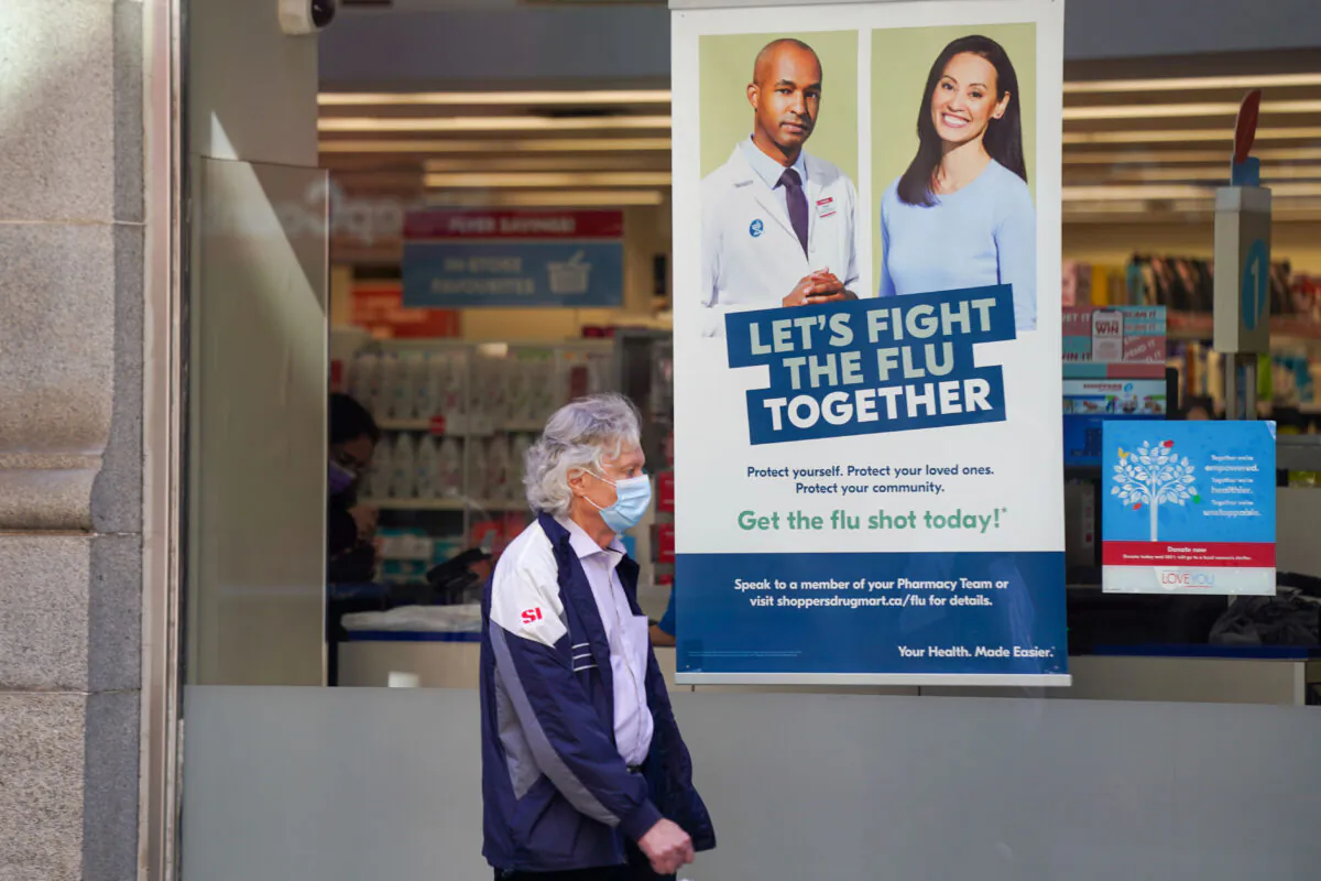 A pedestrian walks by a sign in a store window encouraging people to receive a seasonal flu shot in Toronto on Oct. 19, 2021. (The Canadian Press/Evan Buhler)