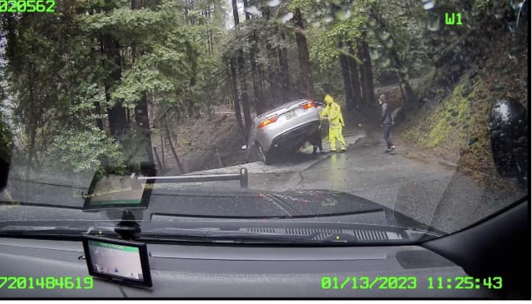 A California Highway Patrol officer helps occupants out of a vehicle trapped on the edge of a cliff in Santa Cruz County, Calif. on Jan. 13, 2023. (Courtesy of California Highway Patrol)