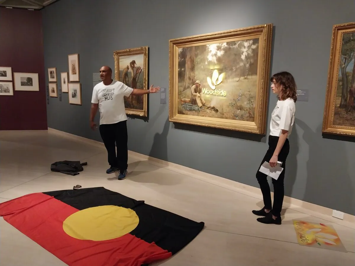 A supplied image shows artists standing beside Frederick McCubbin’s 'Down On His Luck' after launching a faux attack on the famous paintings to protest Woodside’s alleged destruction of rock art, at the Art Gallery of Western Australia in Perth, Australia on Jan. 19, 2023. (AAP Image/Supplied by Disrupt Burrup Hub) 