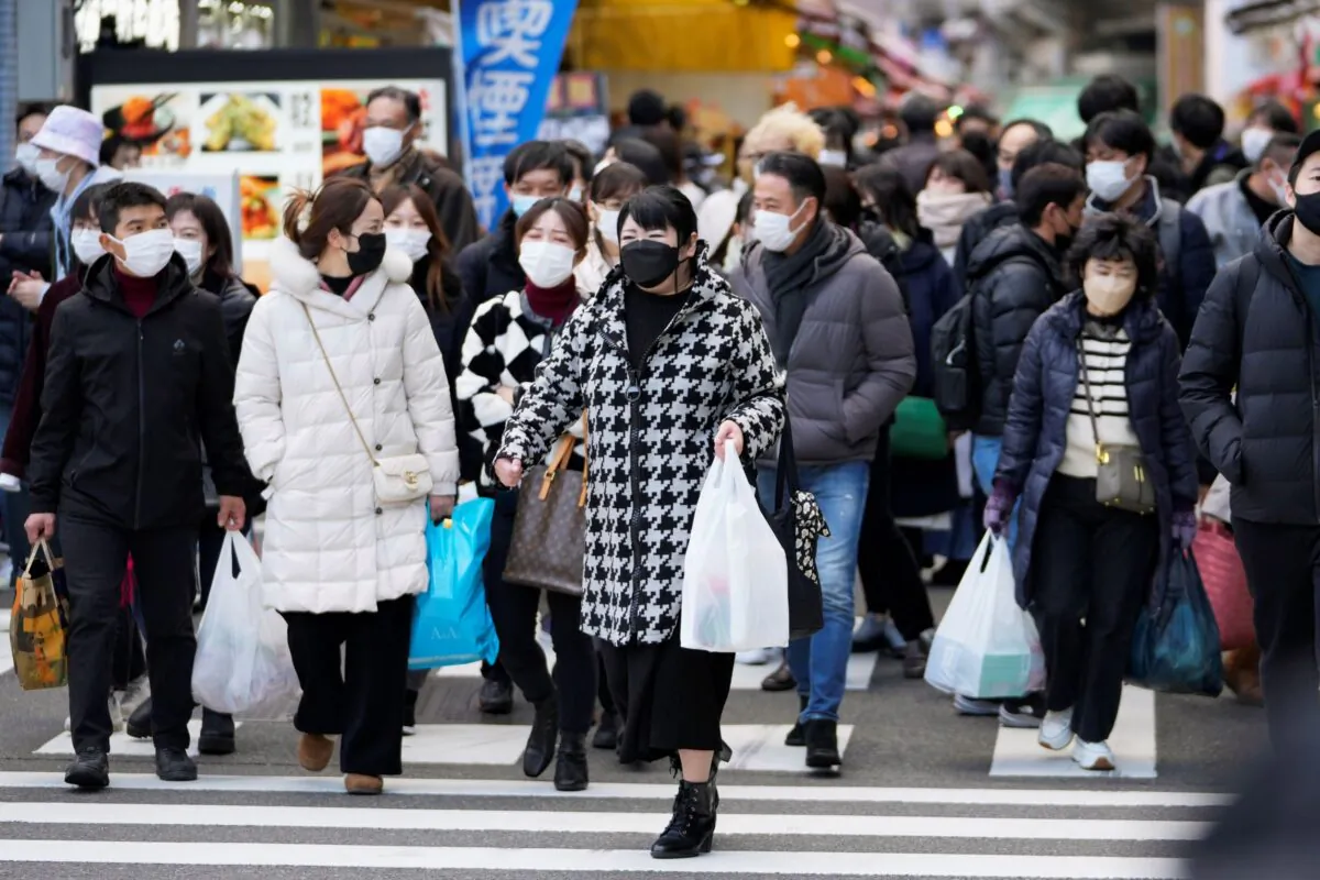 People with shopping bags walk across a traffic intersection towards a train station near a shopping street in the Ueno district in Tokyo on Dec. 30, 2022. (Hiro Komae/AP Photo)
