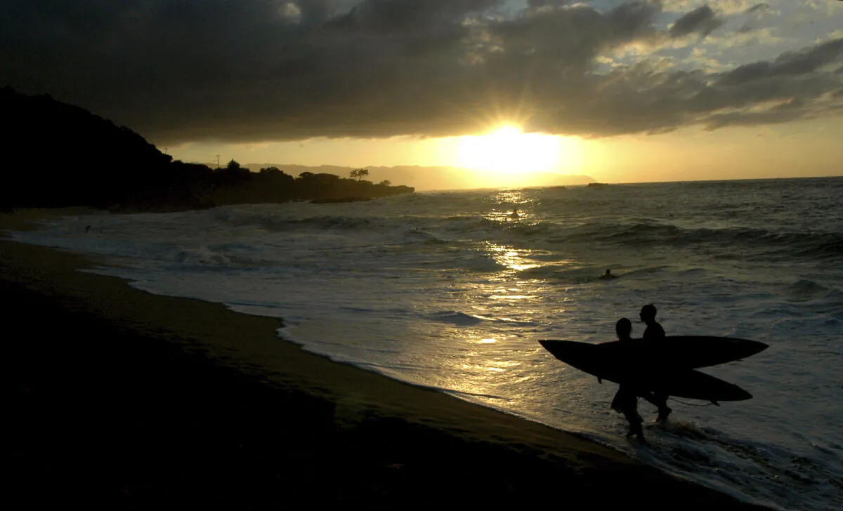 Participants in the In Memory of Eddie Aikau walk out of the ocean at sunset after the opening ceremony in Waimea Bay near Haleiwa, Hawaii, on Nov. 30, 2006. (Lucy Pemoni/AP Photo)