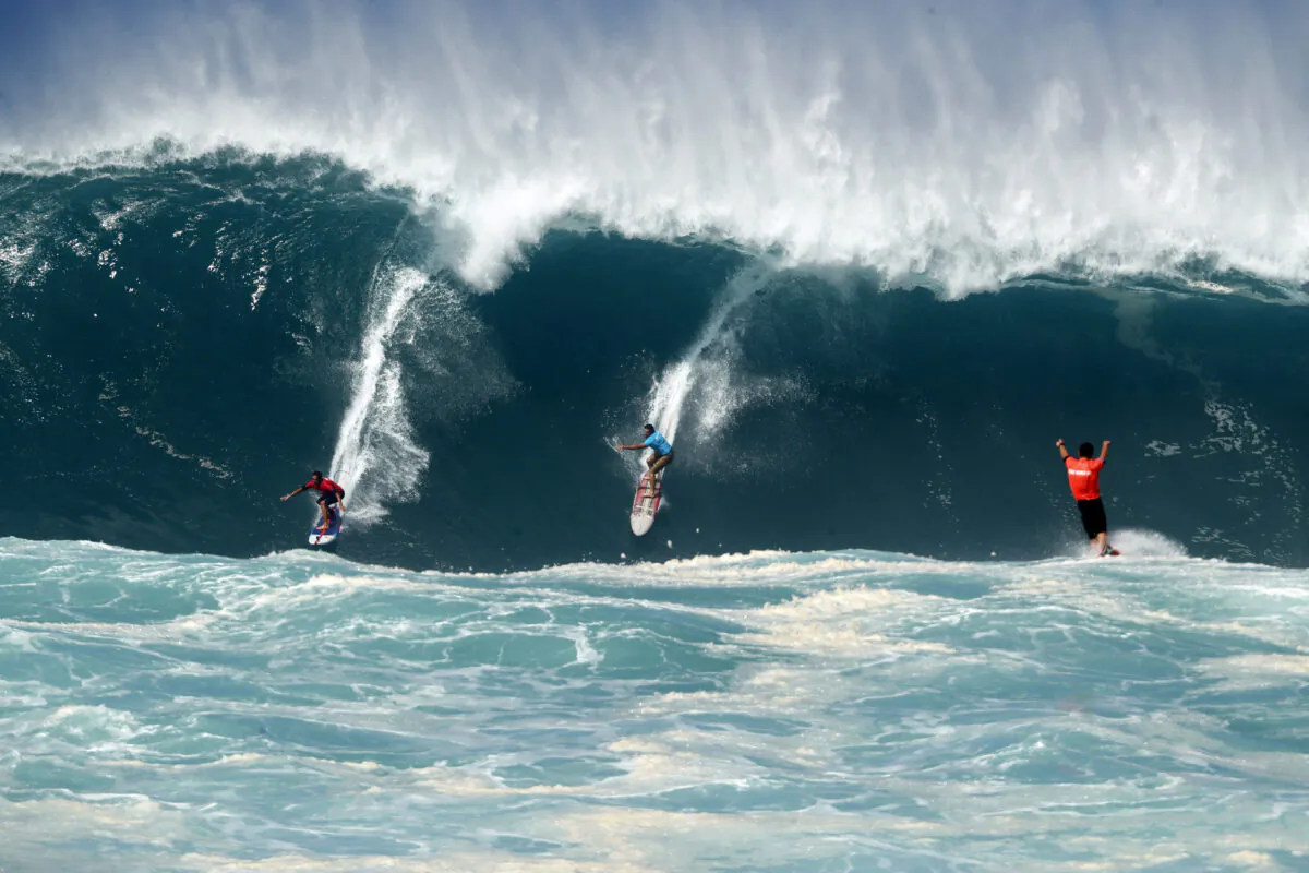 Kai Lenny (L) and Aaron Gold (C) are cheered on by Jake Maki (R) in Hawaii's Waimea Bay on Oahu’s North Shore during the The Eddie Aikau Big Wave Invitational surfing contest on Jan. 22, 2023. (Jamm Aquino/Honolulu Star-Advertiser via AP)