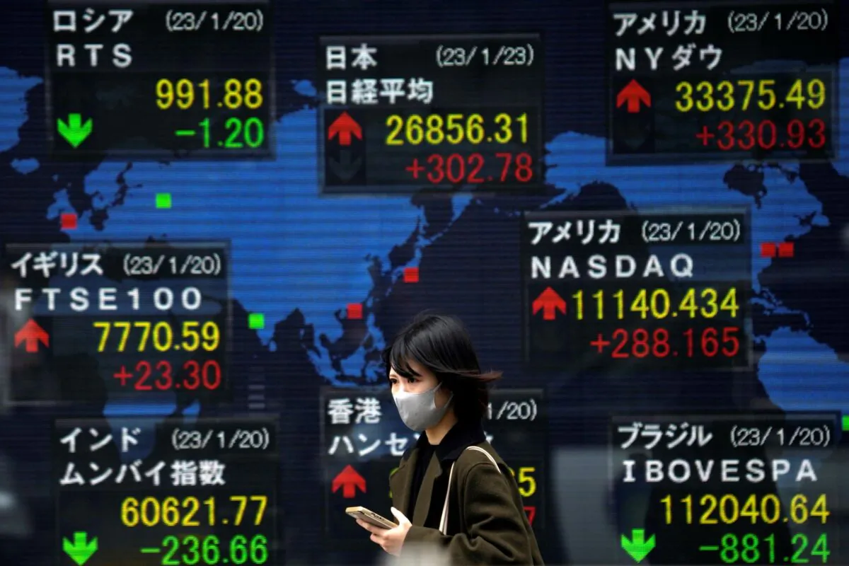 A person wearing a protective mask walks in front of an electronic stock board showing Japan's Nikkei 225 and other indexes at a securities firm, in Tokyo, Japan, on Jan. 23, 2023. (Eugene Hoshiko/AP Photo)