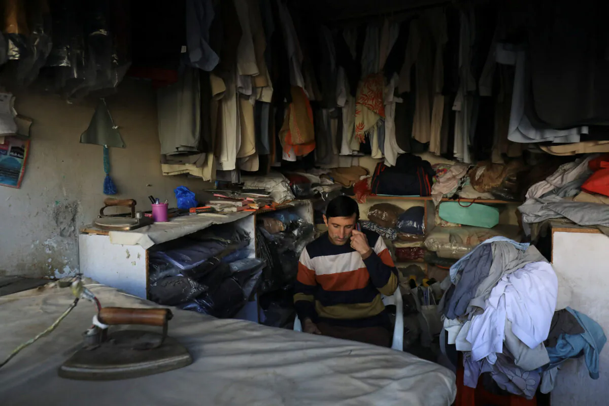 A laundryman uses a cell phone as he sits at his shop during country-wide power breakdown in Peshawar, Pakistan, on Jan. 23, 2023. (Fayaz Aziz/Reuters)