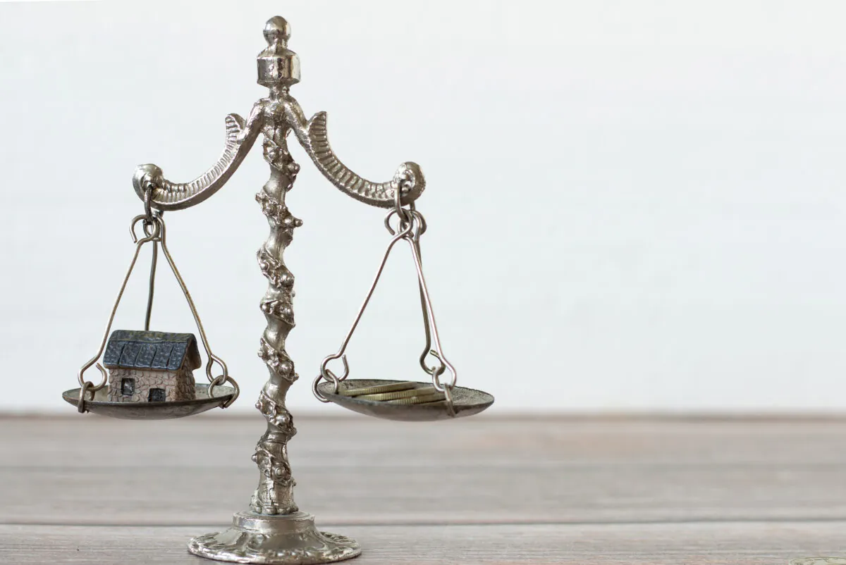 Vintage balance scales with a small house on one side and a few gold coins on the other side. (MarinelaM/Shutterstock)