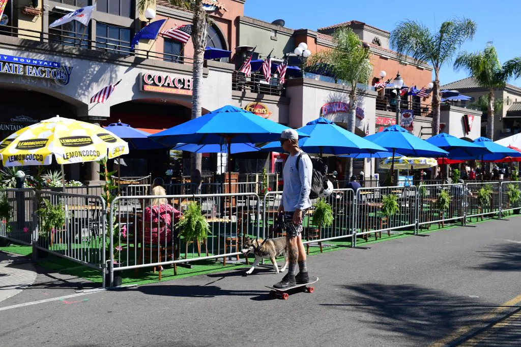 A man on a skateboard rides by outdoor restaurant seating in Huntington Beach, Calif., on July 16, 2020. (Robyn Beck/AFP via Getty Images)