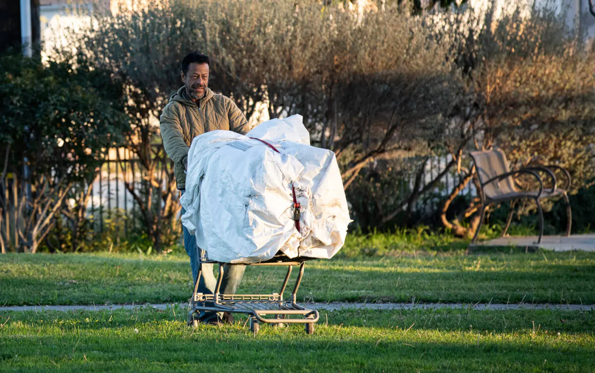 A homeless man pushes a shopping cart through a park in Fullerton, Calif., on Feb. 1, 2023. (John Fredricks/The Epoch Times)