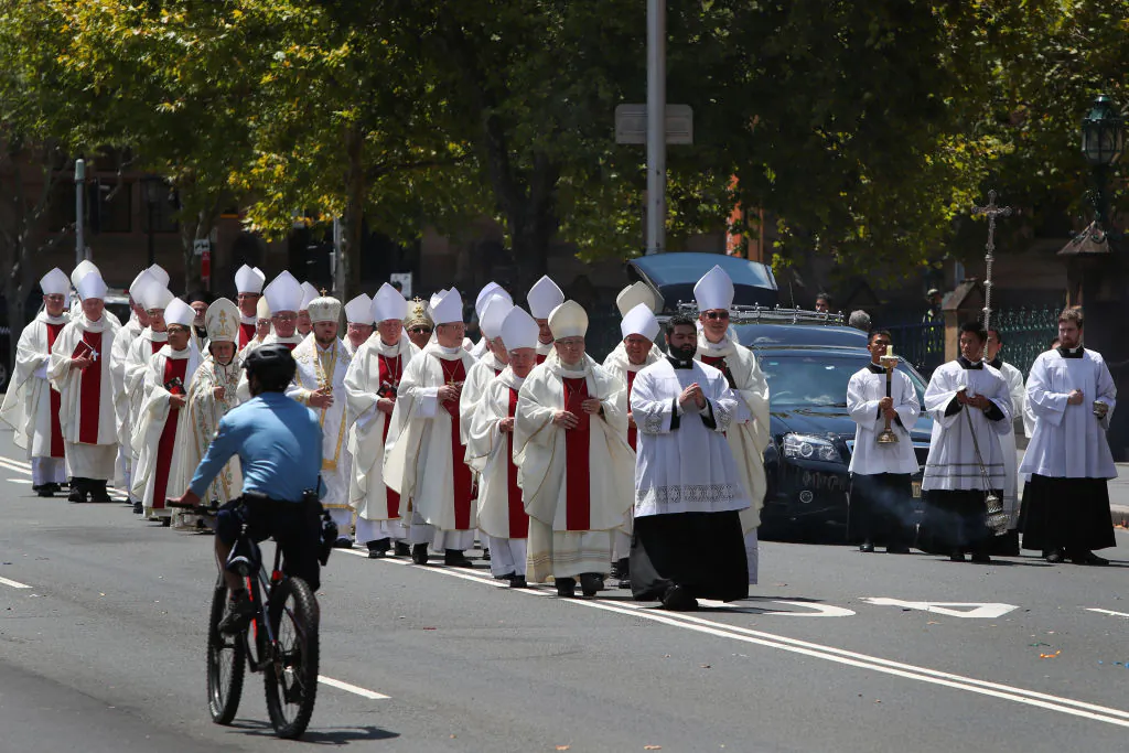 SYDNEY, AUSTRALIA - FEBRUARY 02: A police officer cycles past members of the church forming a procession leading the hearse carrying Cardinal George Pell outside St. Mary’s Cathedral on February 02, 2023 in Sydney, Australia. Cardinal George Pell, a former senior Catholic Church official who was accused of sexual violence in Australia and then cleared, died on 10 January 2023 aged 81 years old. His body was returned to Sydney after his funeral at the Vatican and will lie in state at St. Mary's Cathedral on Feb. 1 and 2. (Photo by Lisa Maree Williams/Getty Images)
