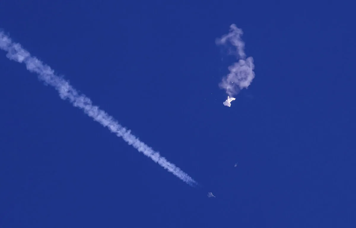 The remnants of a large balloon drift above the Atlantic Ocean, just off the coast of South Carolina, with a fighter jet and its contrail seen below it, on Feb. 4, 2023. (Chad Fish via AP)